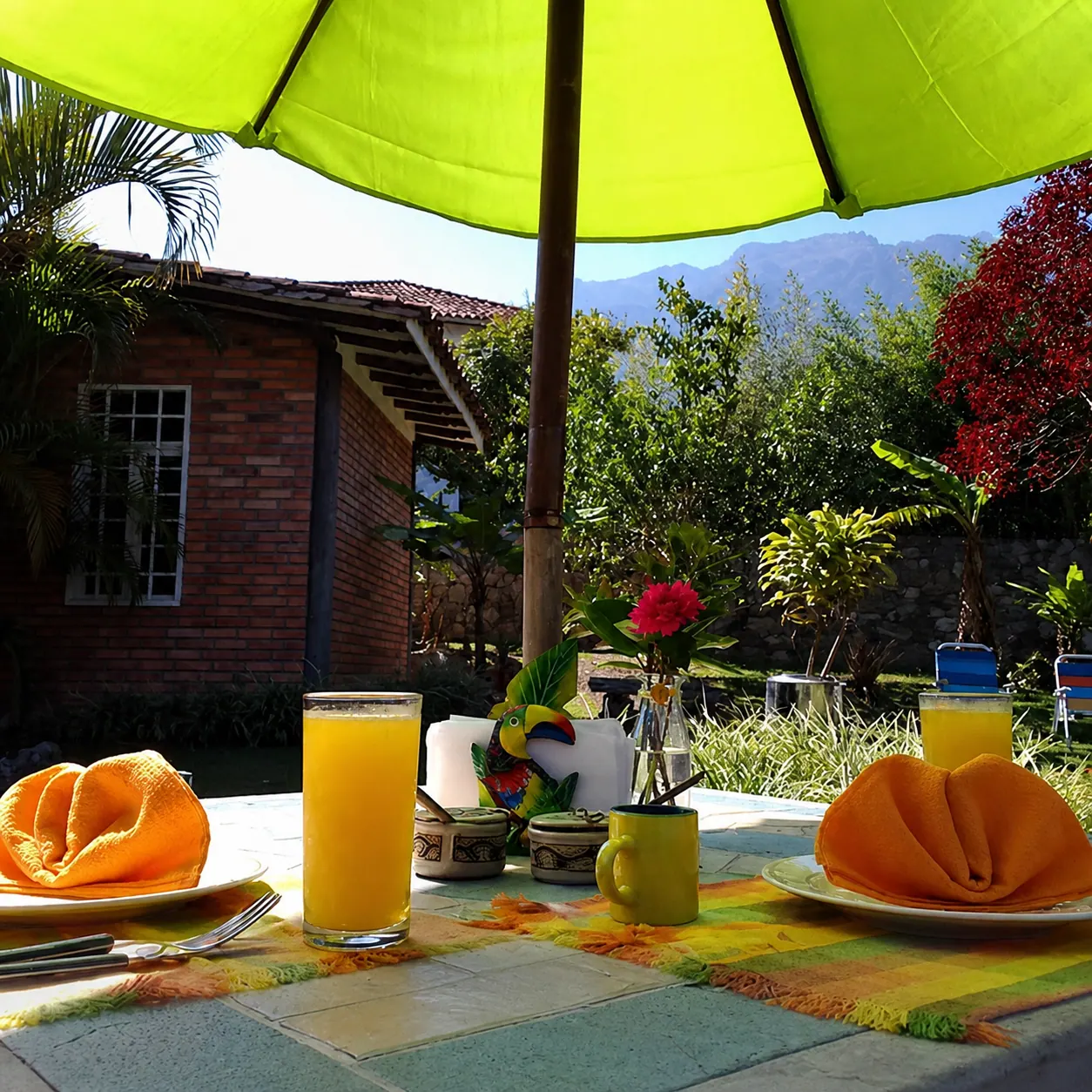 Terraza cubierta con mesa, banquetas y decoración artesanal frente a ventanas blancas