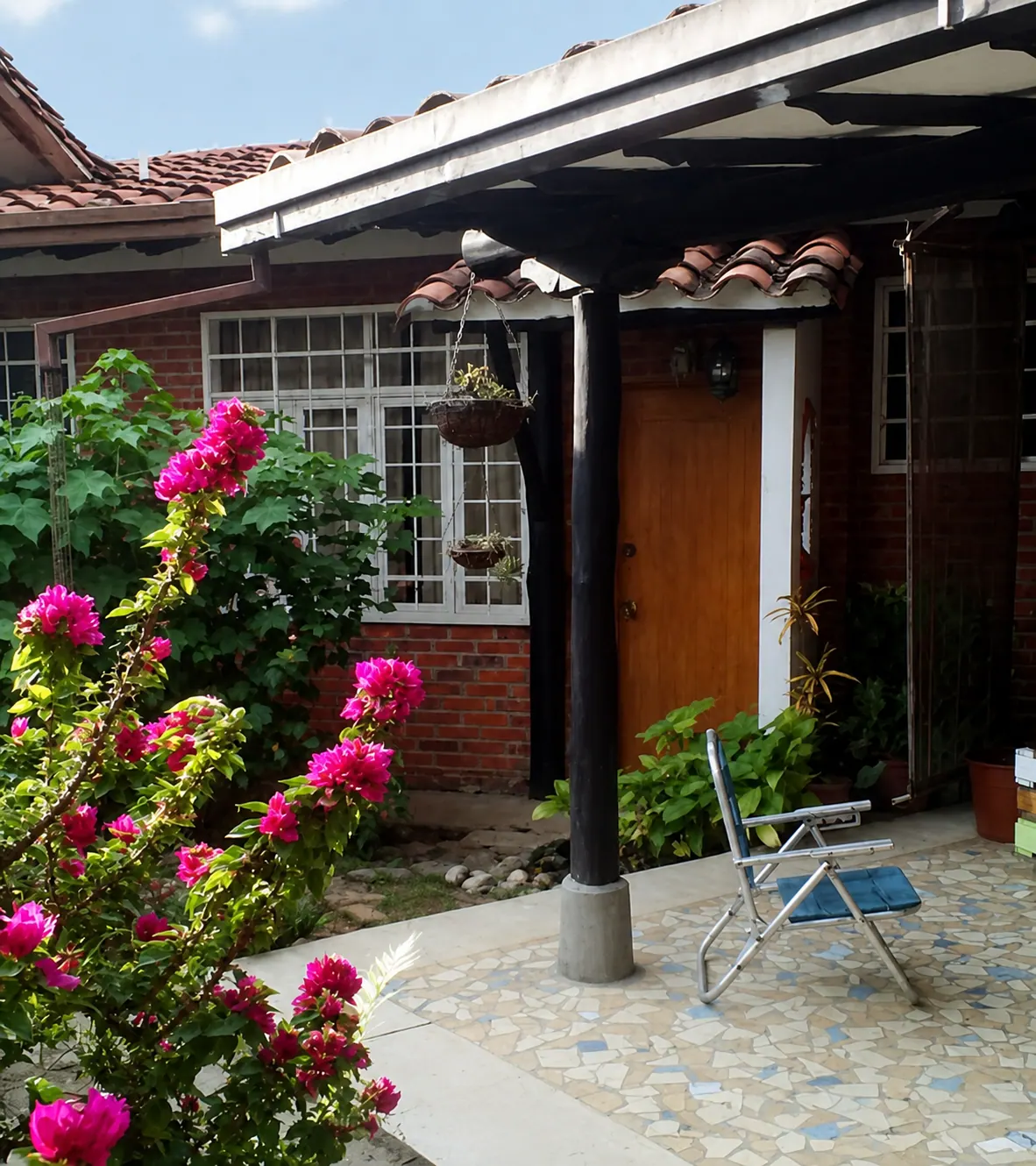 Entrada de ladrillo de La Tucanera con flores fucsias y silla junto al corredor