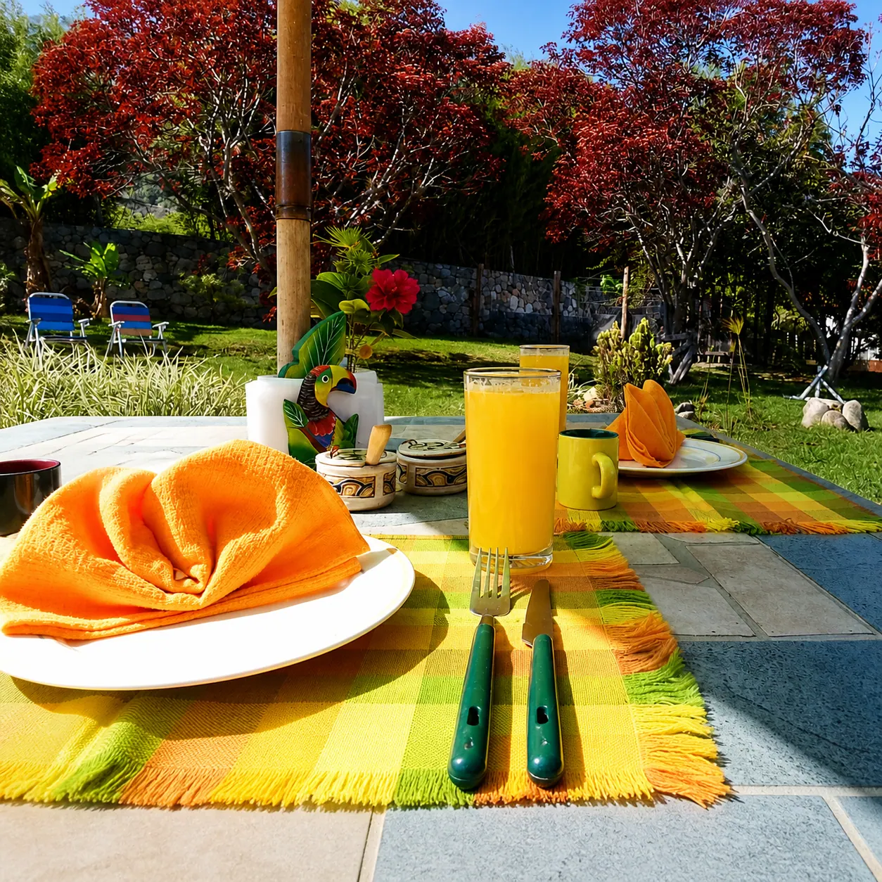 Mesa servida con jugo, servilletas naranjas y vista al jardín de La Tucanera