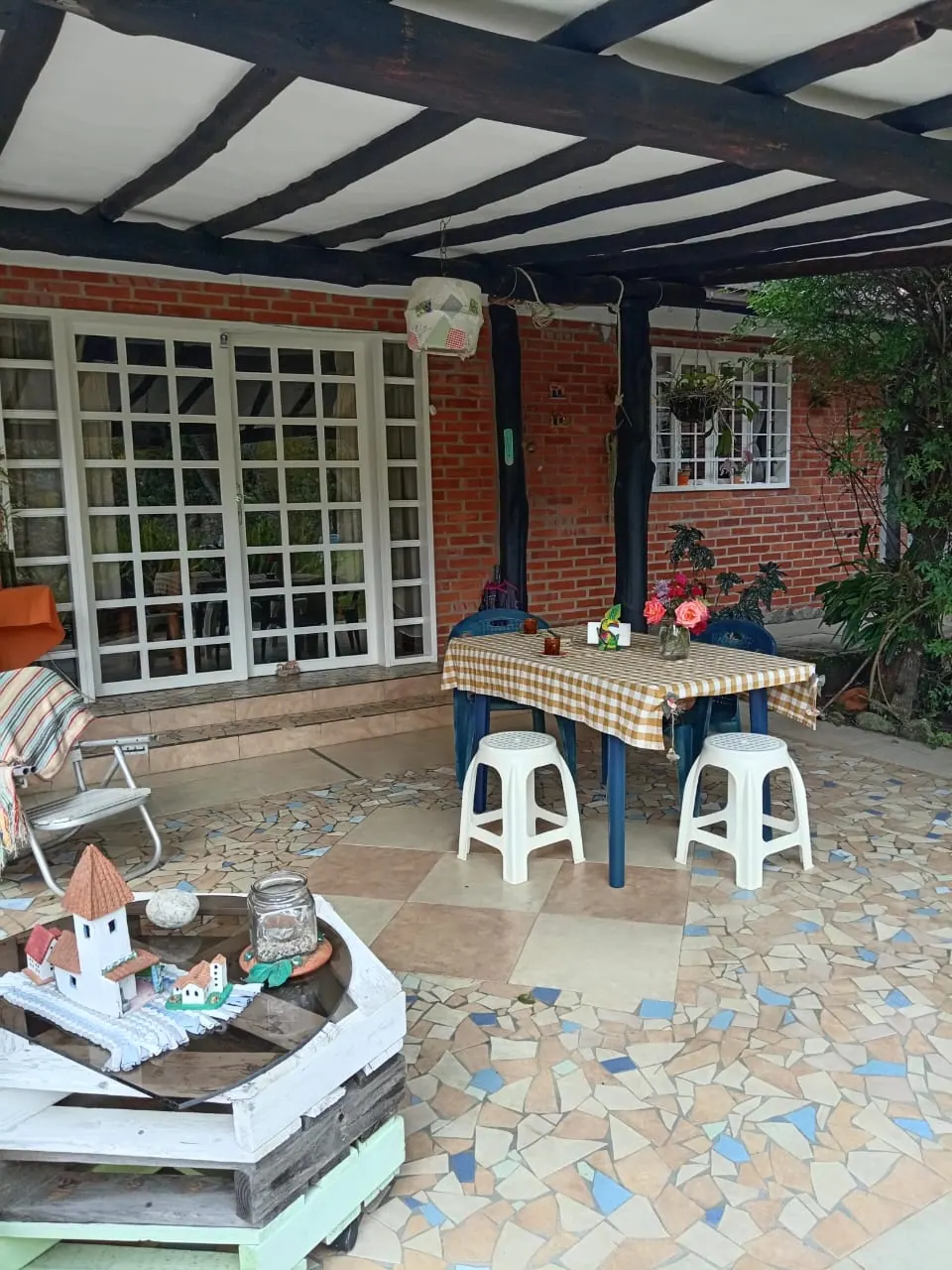 Terraza amplia con mesa, sillas y detalle de casa andina en miniatura