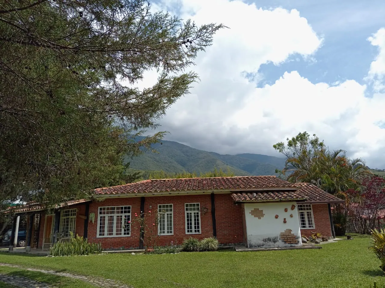 Fachada completa de La Tucanera con jardín amplio y montañas verdes detrás