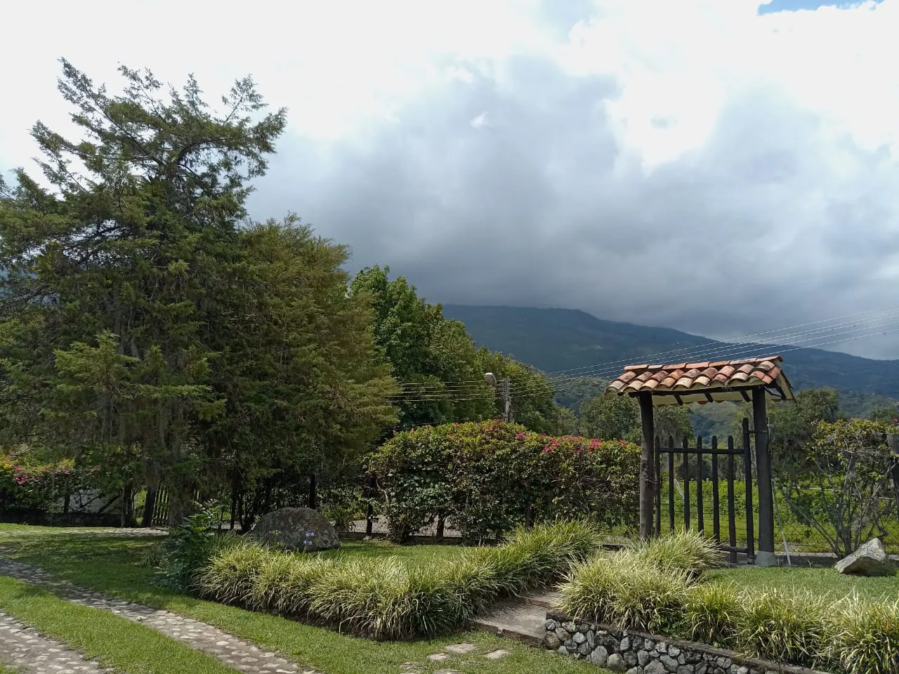 Jardín con cuarto blanco, camino de piedra y montañas bajo nubes densas